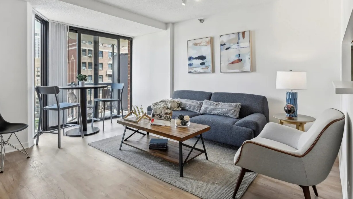 Cozy living area with sofa, accent chair, and café table by sliding doors to a private balcony at 1133 N Dearborn apartments in Chicago
