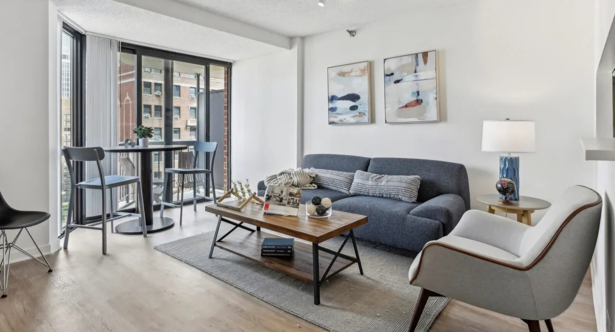 Cozy living area with sofa, accent chair, and café table by sliding doors to a private balcony at 1133 N Dearborn apartments in Chicago