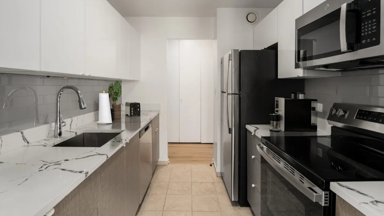 Updated galley kitchen featuring white gloss cabinets, subway backsplash, stainless appliances, and marble-style counters at 1133 N Dearborn in Chicago