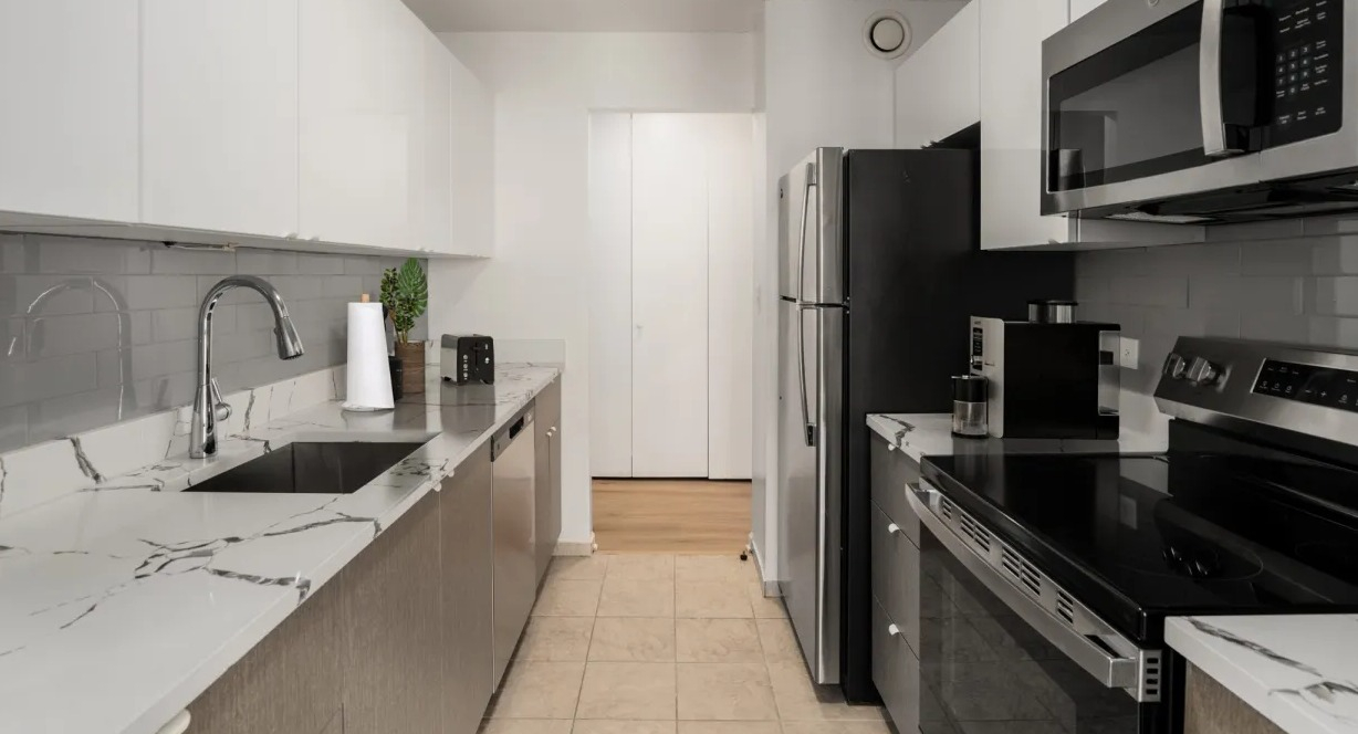 Updated galley kitchen featuring white gloss cabinets, subway backsplash, stainless appliances, and marble-style counters at 1133 N Dearborn in Chicago