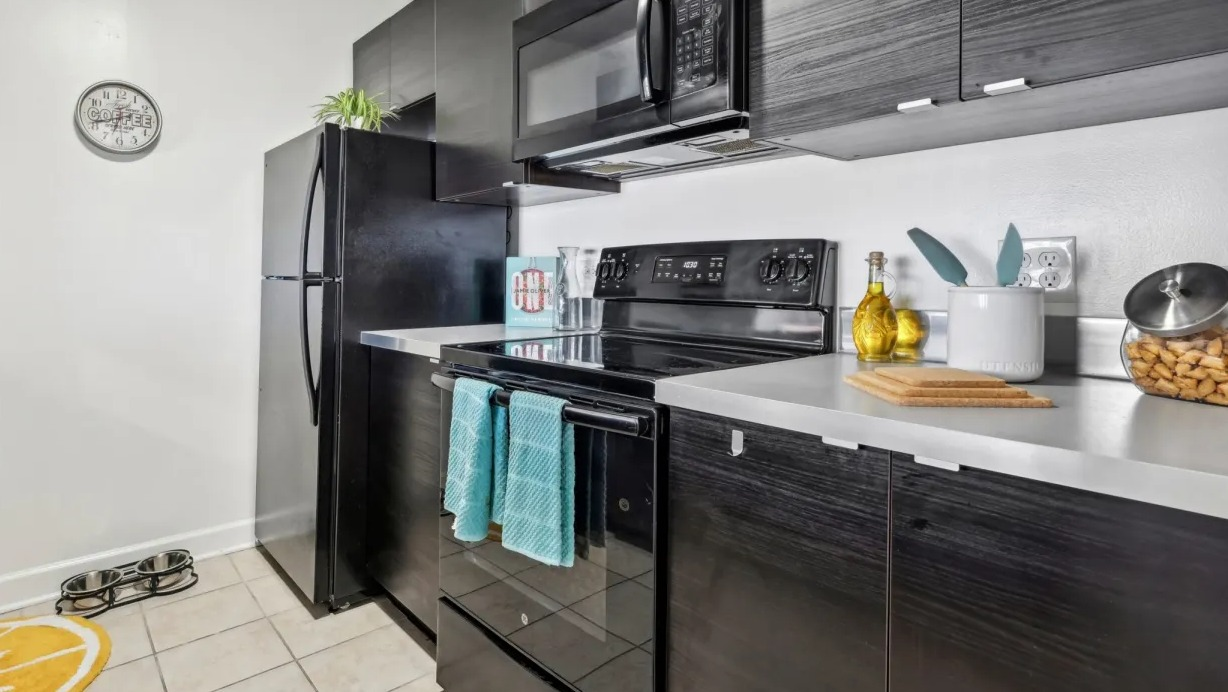 Contemporary kitchen featuring dark wood-look cabinets, black appliances, light countertops, and tiled floor at 1133 N Dearborn apartments in Chicago