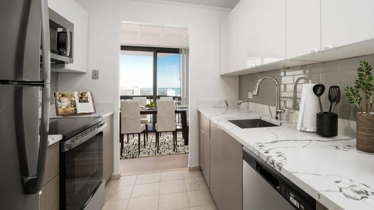 Modern galley kitchen with sleek white cabinetry, stone counters, and view toward the dining area and balcony at 1133 N Dearborn apartments in Chicago