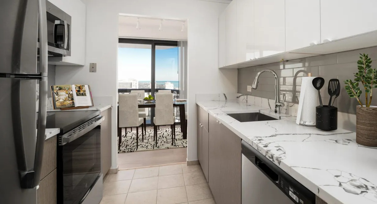 Modern galley kitchen with sleek white cabinetry, stone counters, and view toward the dining area and balcony at 1133 N Dearborn apartments in Chicago
