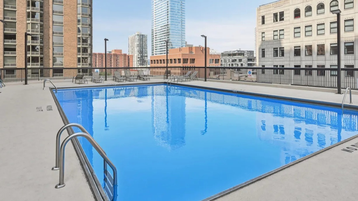 Outdoor swimming pool with lounge seating and skyline views surrounded by neighboring high-rises at 1133 N Dearborn apartments in Chicago