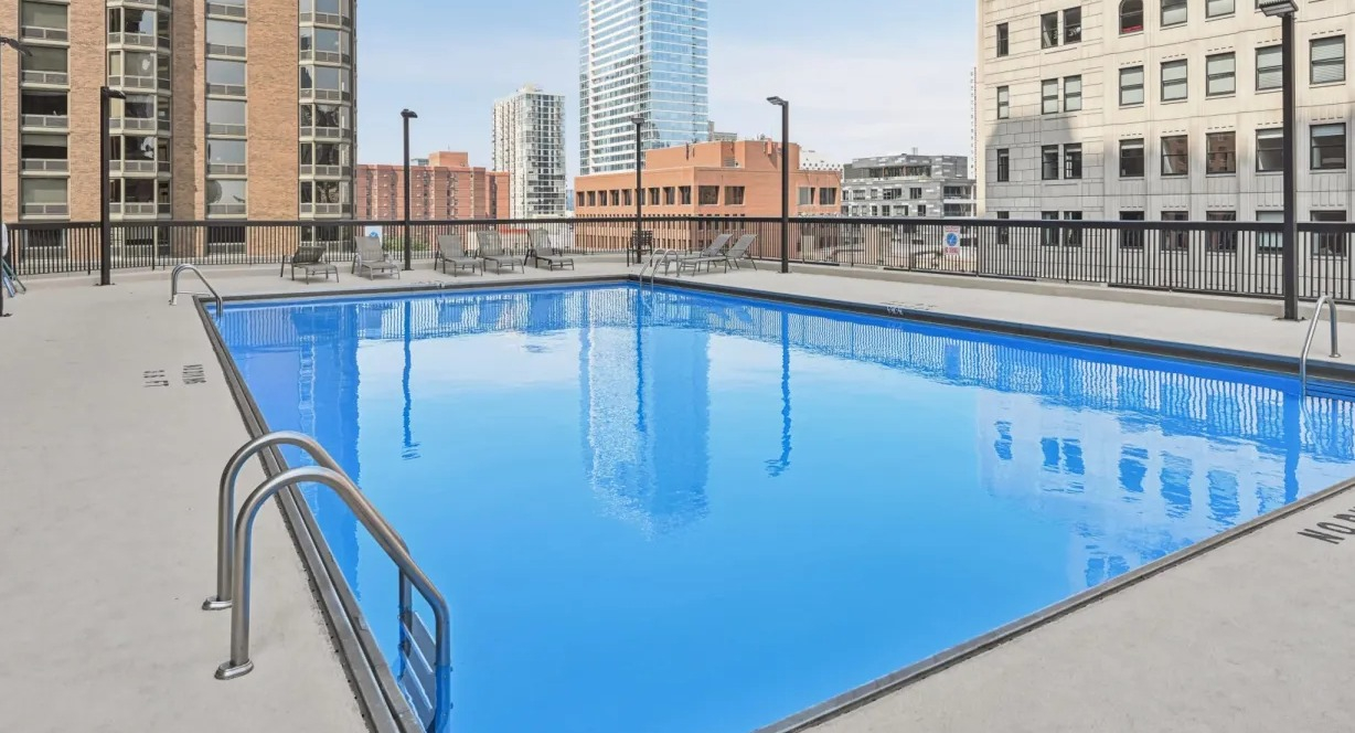 Outdoor swimming pool with lounge seating and skyline views surrounded by neighboring high-rises at 1133 N Dearborn apartments in Chicago