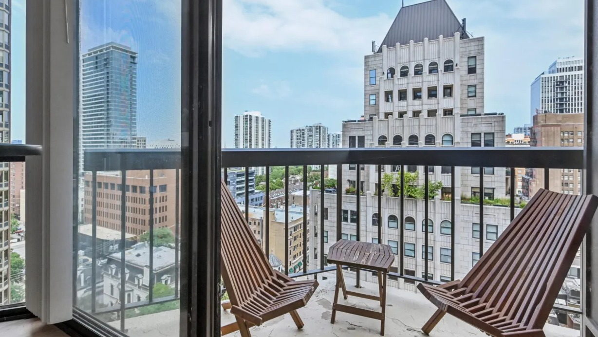Private balcony with two lounge chairs and a small table overlooking classic and modern Chicago architecture at 1133 N Dearborn apartments