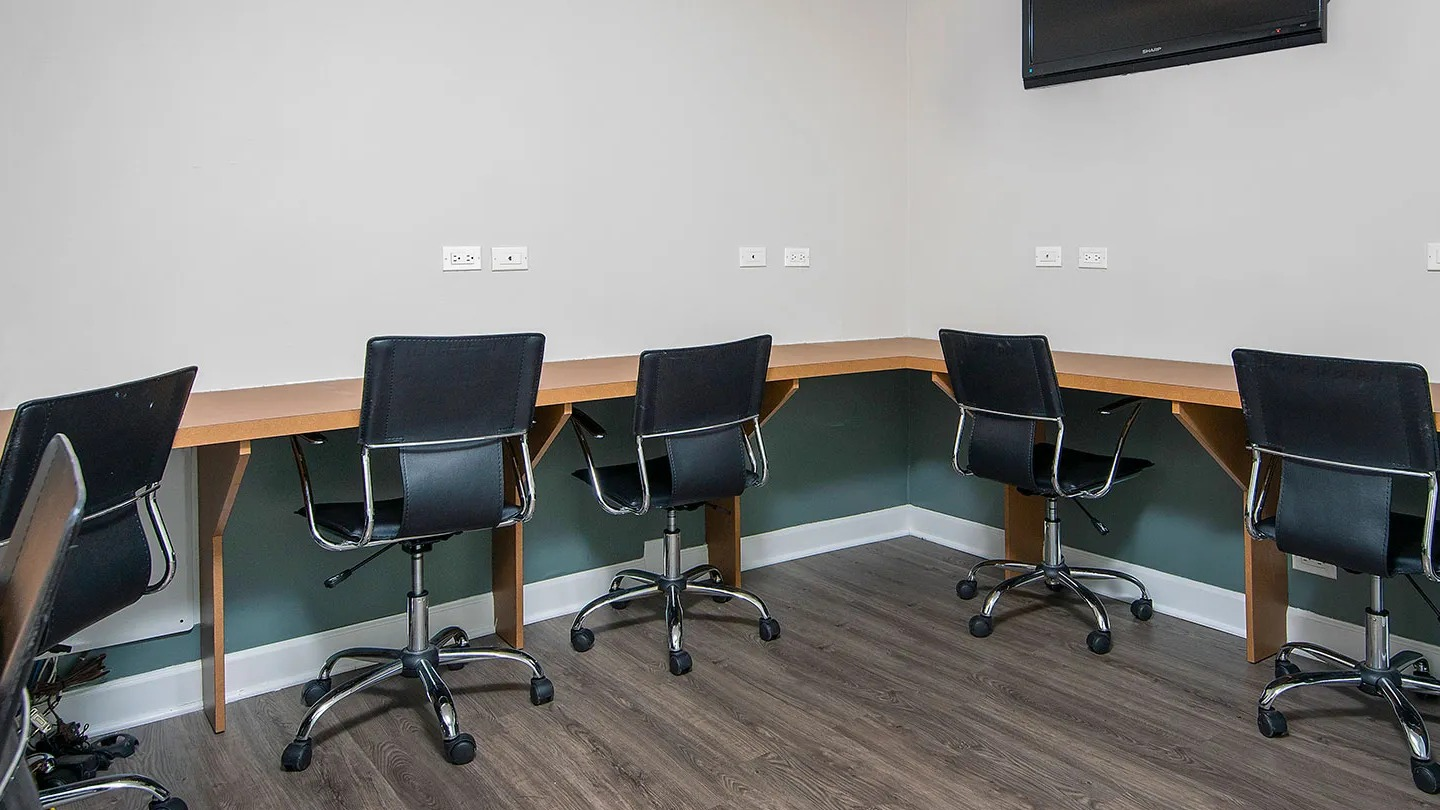 Resident business center with built-in desks, task chairs, outlets, and wall-mounted TV offering a quiet workspace at 1133 N Dearborn apartments in Chicago