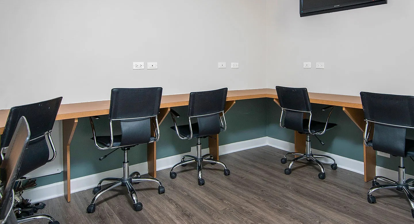 Resident business center with built-in desks, task chairs, outlets, and wall-mounted TV offering a quiet workspace at 1133 N Dearborn apartments in Chicago
