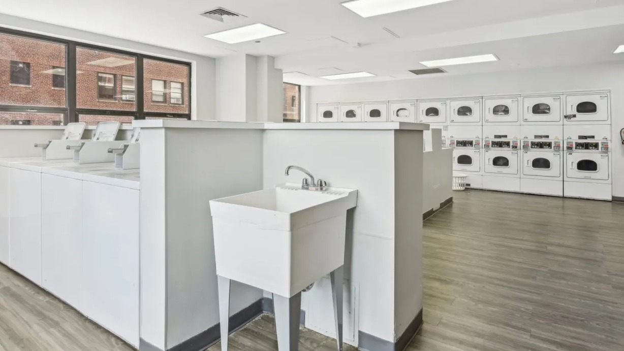 Bright resident laundry room with rows of washers and dryers, folding counters, utility sink, and vinyl floors at 1133 N Dearborn apartments in Chicago