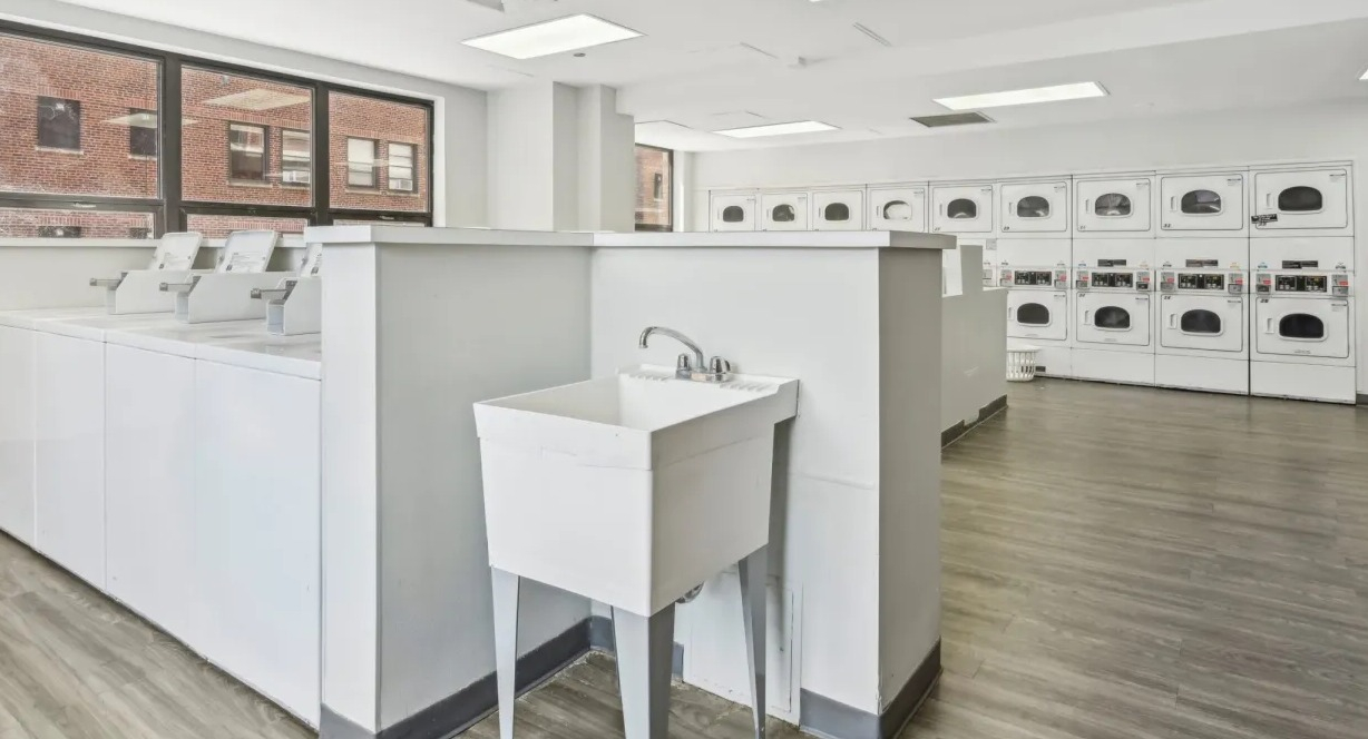 Bright resident laundry room with rows of washers and dryers, folding counters, utility sink, and vinyl floors at 1133 N Dearborn apartments in Chicago