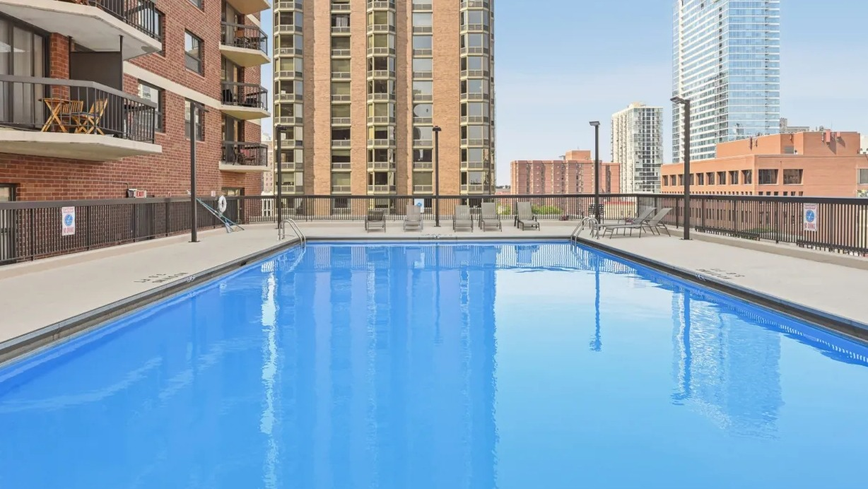 Spacious rooftop pool deck with clear blue water, seating areas, and views of nearby towers for summer relaxation at 1133 N Dearborn apartments in Chicago