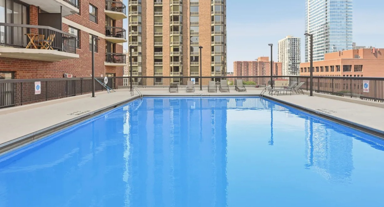 Spacious rooftop pool deck with clear blue water, seating areas, and views of nearby towers for summer relaxation at 1133 N Dearborn apartments in Chicago
