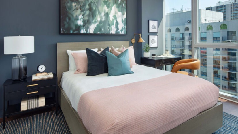 Bedroom with floor-to-ceiling windows, city views, and layered bedding in soft tones at 1225 Old Town Apartments in Chicago