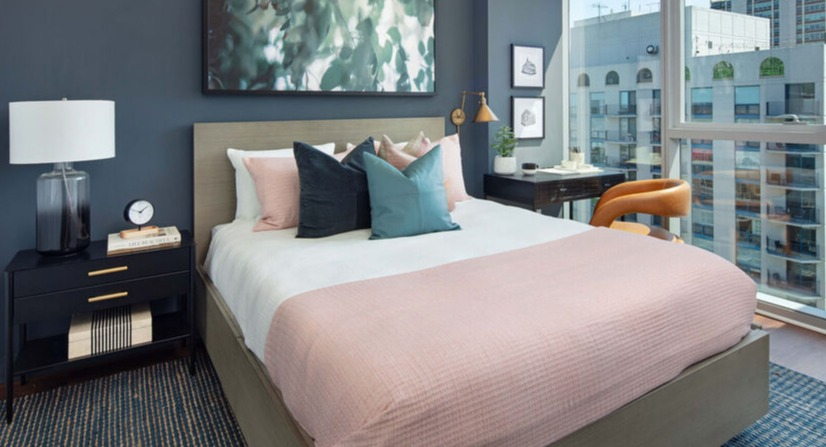 Bedroom with floor-to-ceiling windows, city views, and layered bedding in soft tones at 1225 Old Town Apartments in Chicago