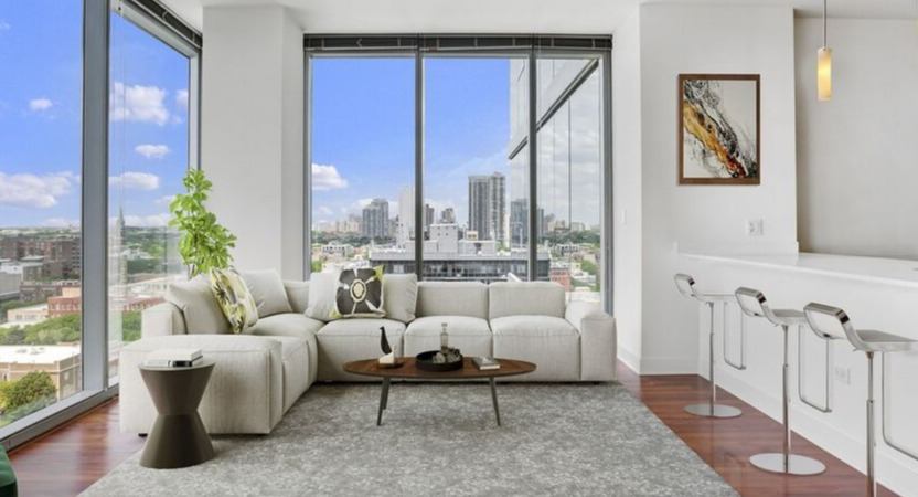 Corner living room with floor-to-ceiling windows, white sectional, and breakfast bar seating showcasing skyline views at 1225 Old Town Apartments in Chicago