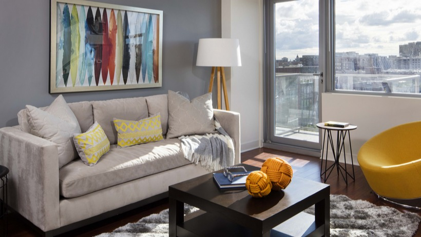 Cozy living room with grey accent wall, plush sofa, yellow chair, and balcony door bringing daylight at 1225 Old Town Apartments in Chicago