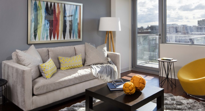 Cozy living room with grey accent wall, plush sofa, yellow chair, and balcony door bringing daylight at 1225 Old Town Apartments in Chicago