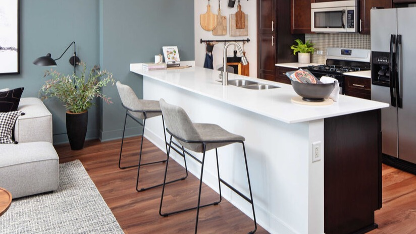 Designer kitchen with breakfast bar, pendant lights, dark cabinetry, and stainless appliances next to a cozy living area at 1225 Old Town Apartments in Chicago