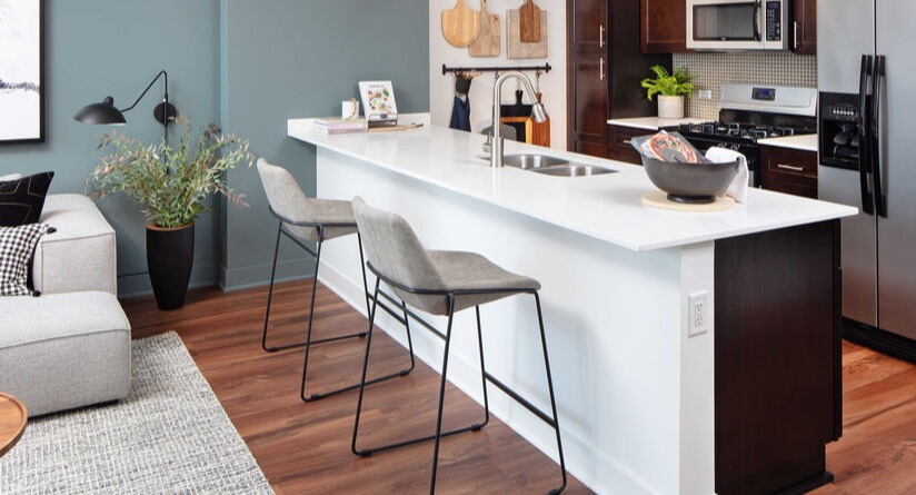 Designer kitchen with breakfast bar, pendant lights, dark cabinetry, and stainless appliances next to a cozy living area at 1225 Old Town Apartments in Chicago