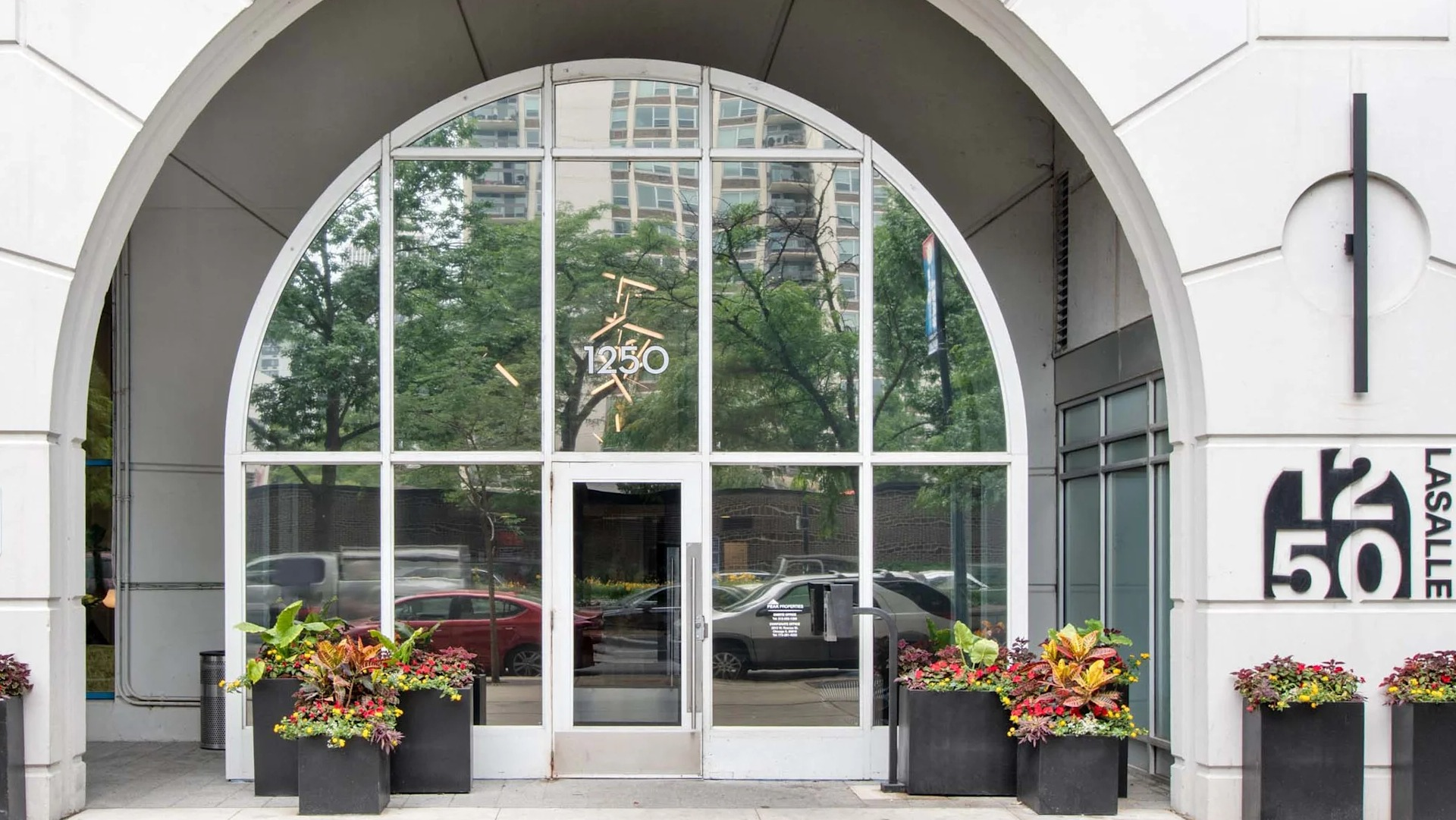 Grand arched entrance of 1250 LaSalle in Chicago with tall glass doors, building signage, and planters lining the sidewalk for a welcoming arrival