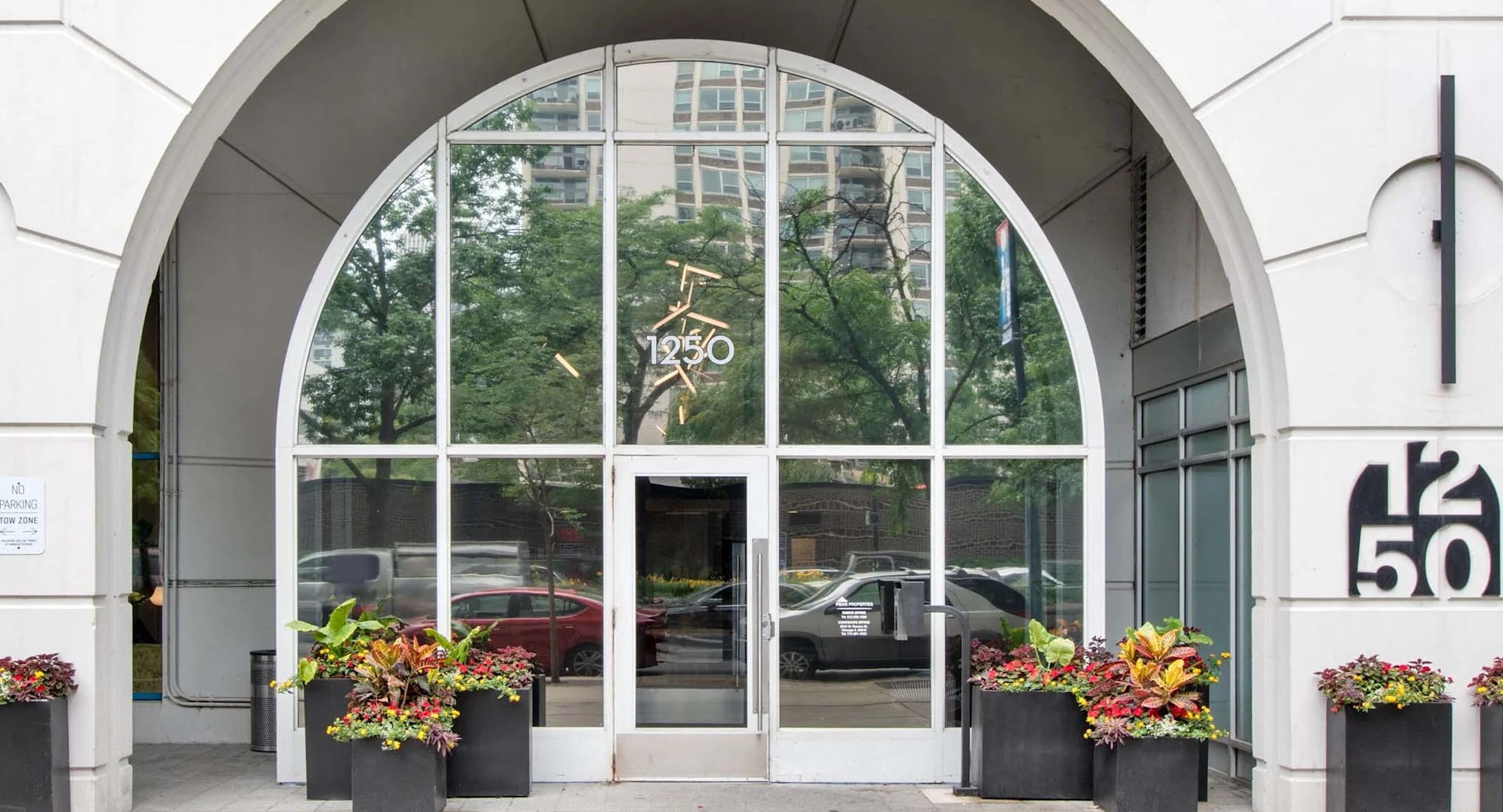 Grand arched entrance of 1250 LaSalle in Chicago with tall glass doors, building signage, and planters lining the sidewalk for a welcoming arrival