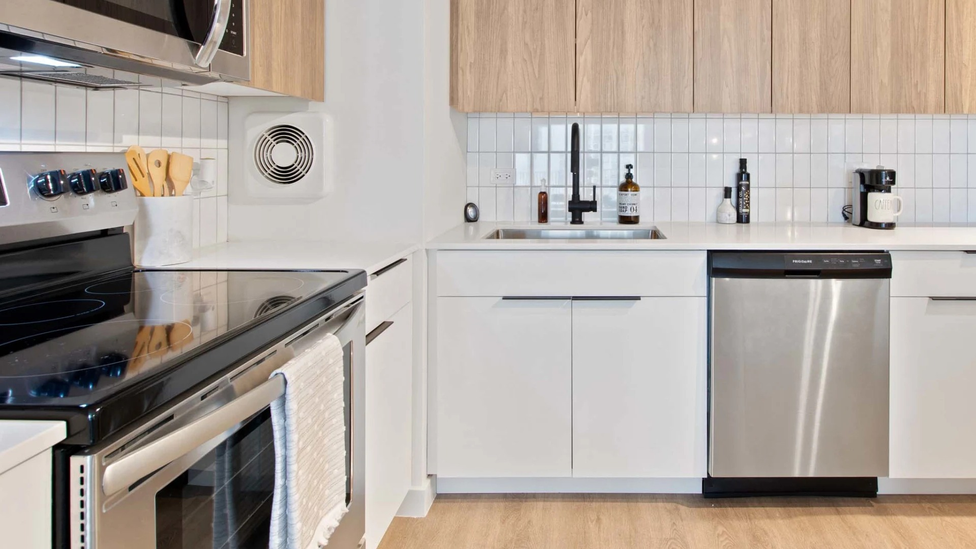 Bright galley kitchen at 1250 LaSalle showcasing stainless dishwasher, deep sink with black faucet, sleek white cabinetry, and quartz counters
