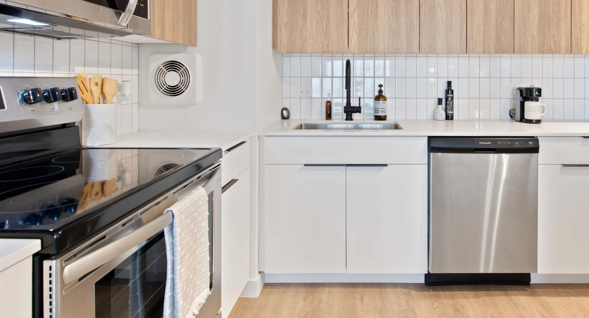 Bright galley kitchen at 1250 LaSalle showcasing stainless dishwasher, deep sink with black faucet, sleek white cabinetry, and quartz counters