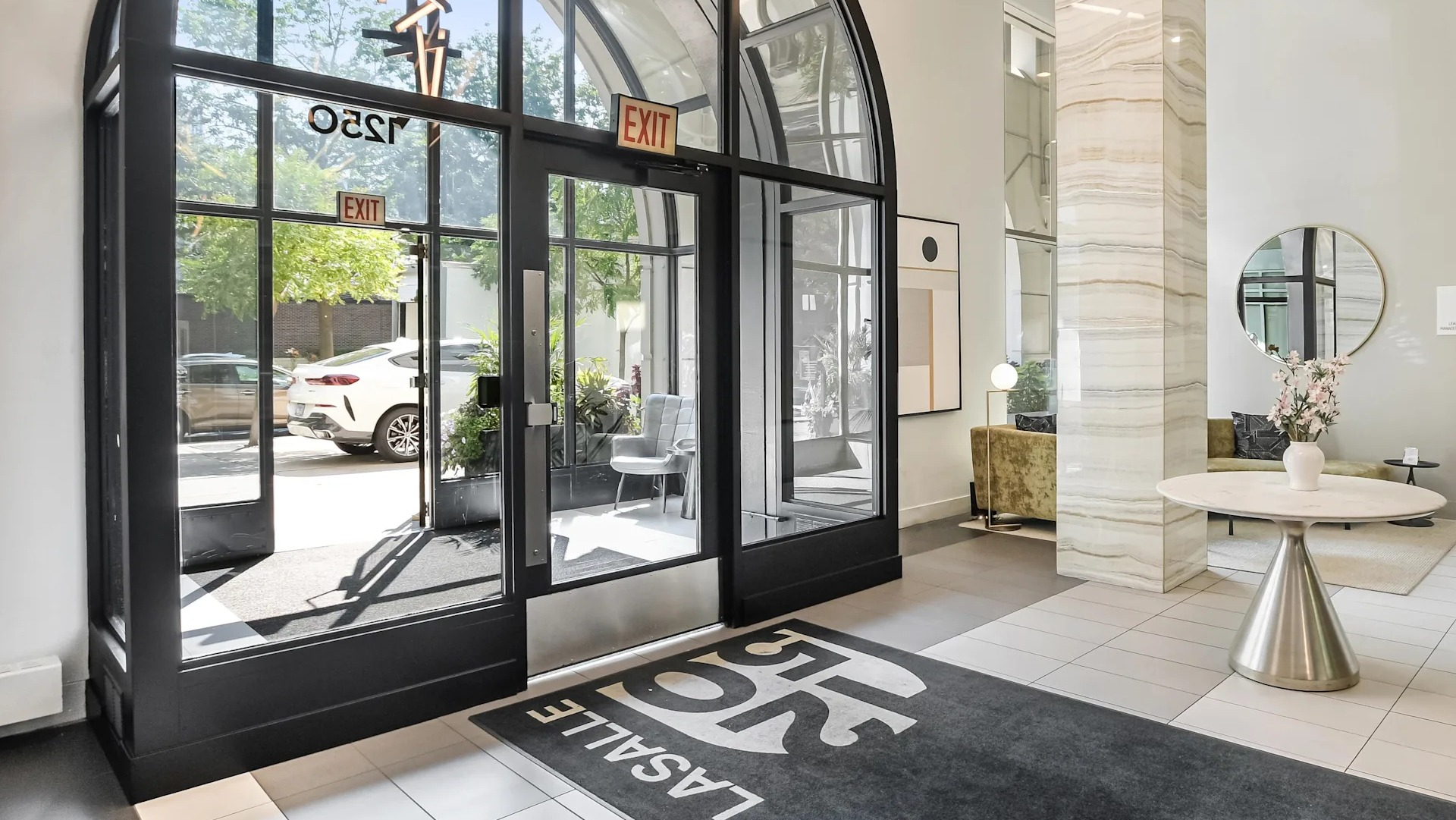 Elegant lobby entrance at 1250 LaSalle featuring dramatic arched glass doors, sculptural lighting, and welcoming seating by bright windows