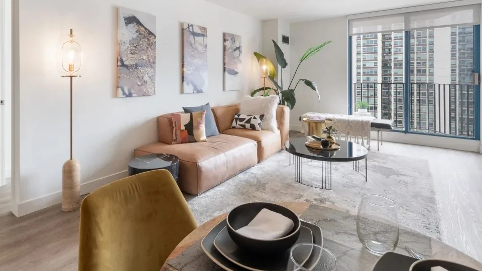 Open living and dining area at 1250 LaSalle in Chicago with a tan sectional, art wall, balcony doors, and shelving for a bright, airy feel