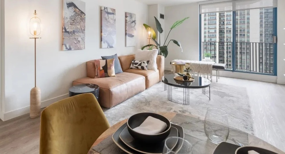 Open living and dining area at 1250 LaSalle in Chicago with a tan sectional, art wall, balcony doors, and shelving for a bright, airy feel
