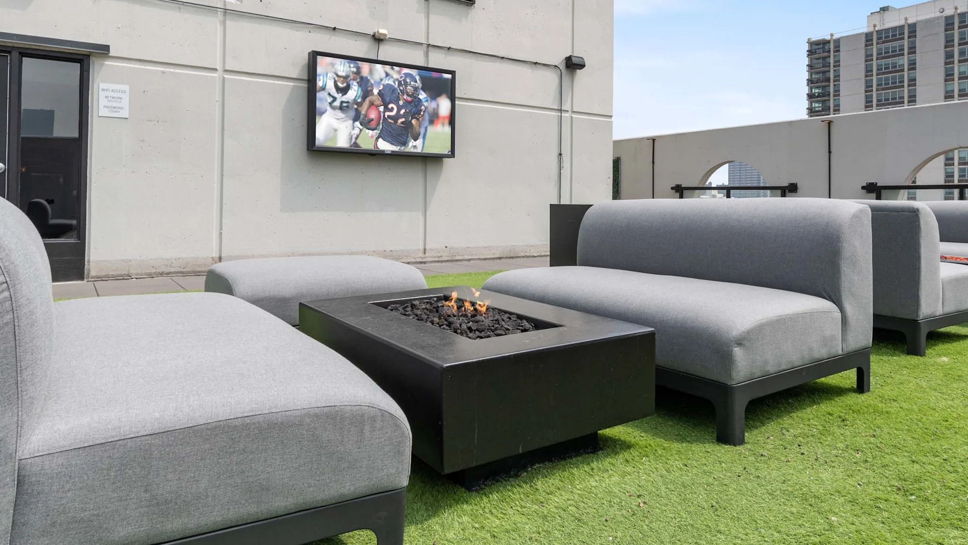 Rooftop lounge at 1250 LaSalle in Chicago featuring cushioned seating around a fire pit on turf with an outdoor TV and nearby high-rise views