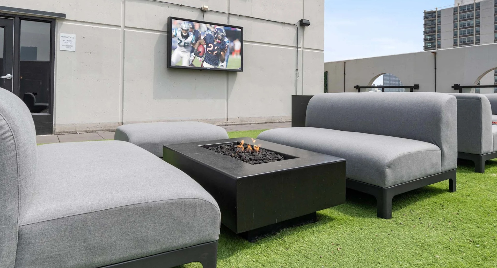 Rooftop lounge at 1250 LaSalle in Chicago featuring cushioned seating around a fire pit on turf with an outdoor TV and nearby high-rise views