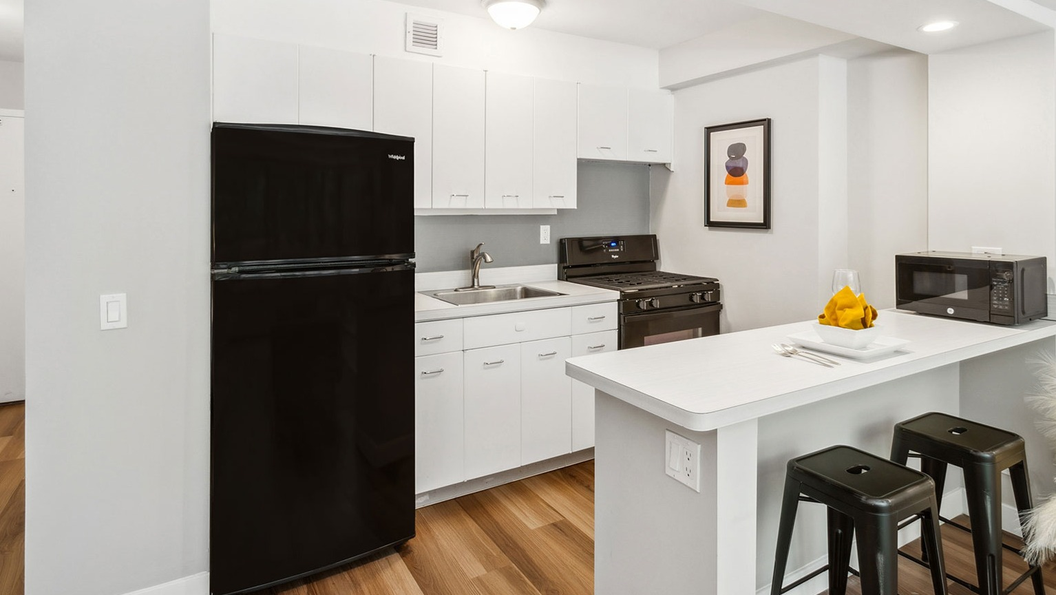 Studio kitchen with white cabinetry, black appliances, and a breakfast bar with seating at 1350–1360 Lake Shore Drive apartments in Chicago
