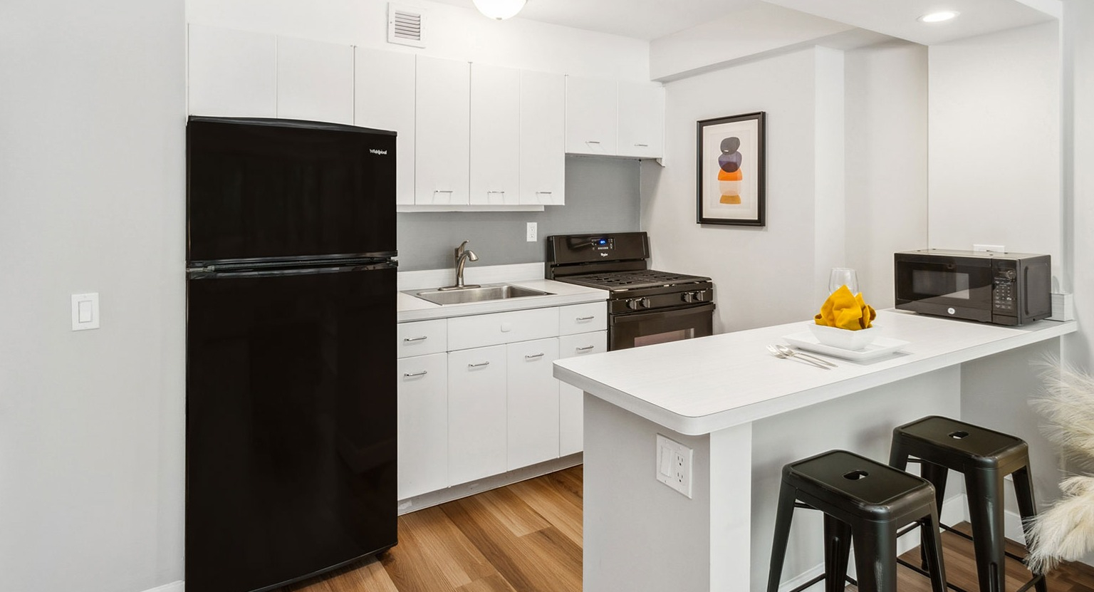 Studio kitchen with white cabinetry, black appliances, and a breakfast bar with seating at 1350–1360 Lake Shore Drive apartments in Chicago
