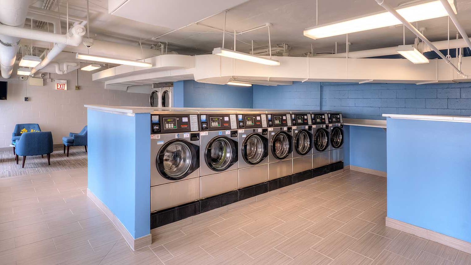 Spacious resident laundry room with rows of front-load washers, folding counters, seating, and bright lighting at 1350-1360 Lake Shore Drive in Chicago