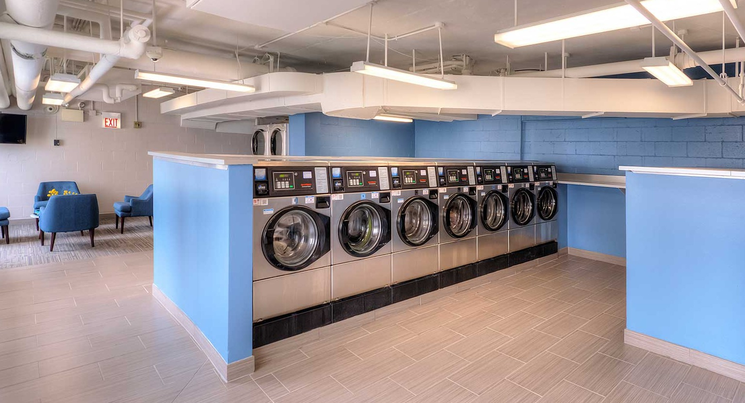 Spacious resident laundry room with rows of front-load washers, folding counters, seating, and bright lighting at 1350-1360 Lake Shore Drive in Chicago