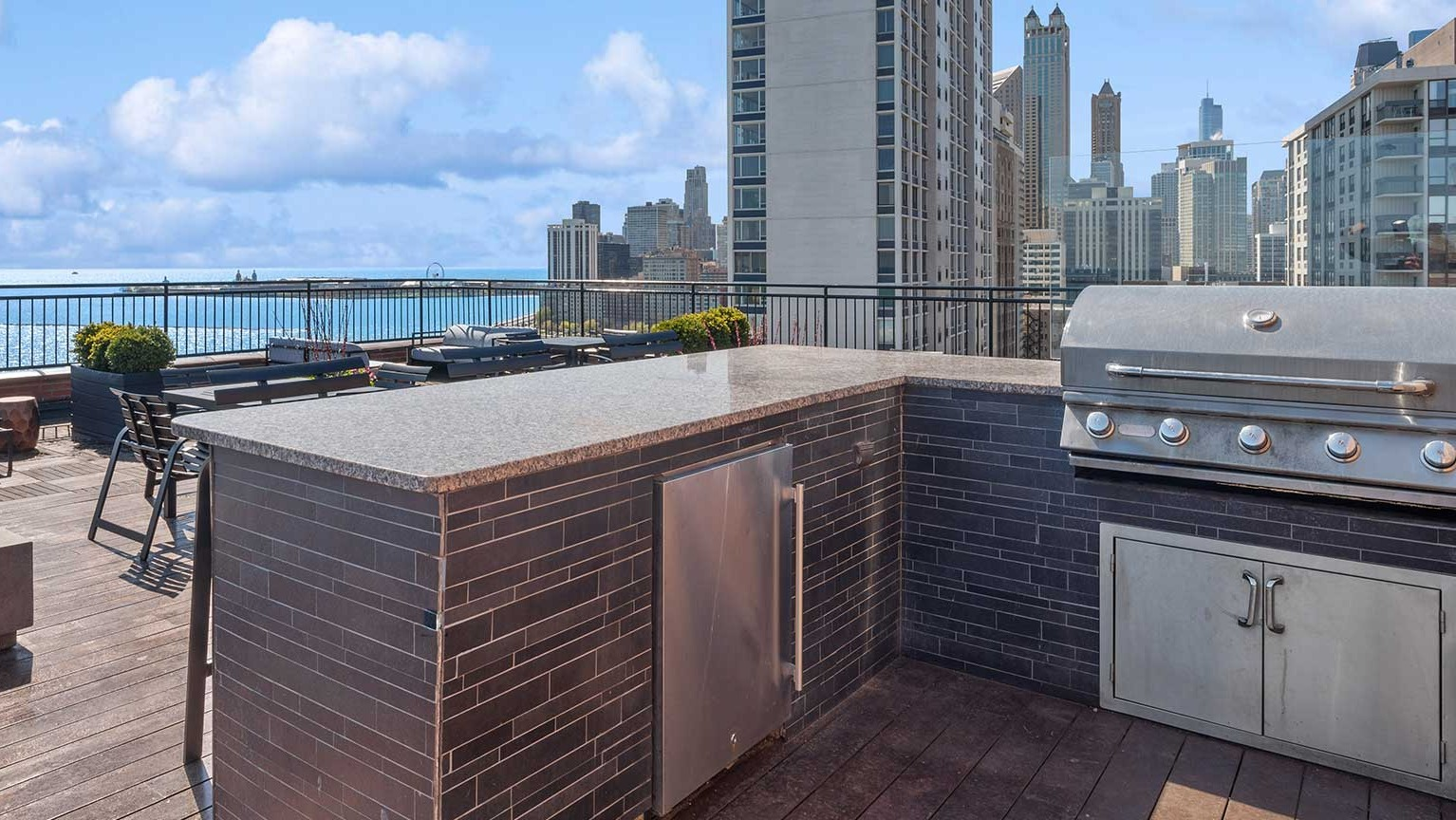 Rooftop grilling station with built-in gas grill, counter space, fire pit seating, and sweeping lake and skyline views at 1350–1360 Lake Shore Drive in Chicago