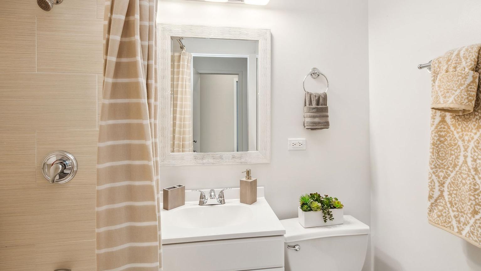 Updated bathroom with tub and shower, beige tile surround, white vanity, framed mirror, and chrome fixtures at 1350–1360 Lake Shore Drive in Chicago