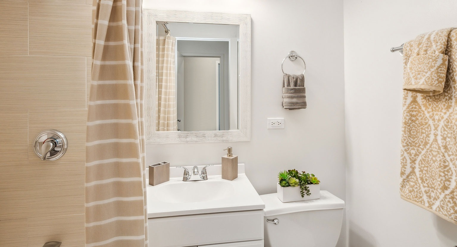 Updated bathroom with tub and shower, beige tile surround, white vanity, framed mirror, and chrome fixtures at 1350–1360 Lake Shore Drive in Chicago