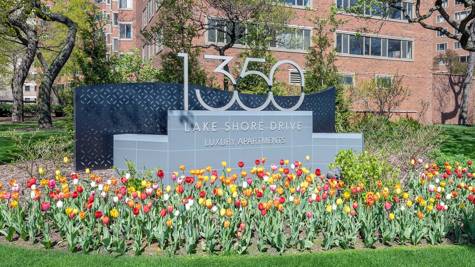 Entrance monument sign for 1350 Lake Shore Drive luxury apartments, framed by blooming tulips and mature trees in Chicago