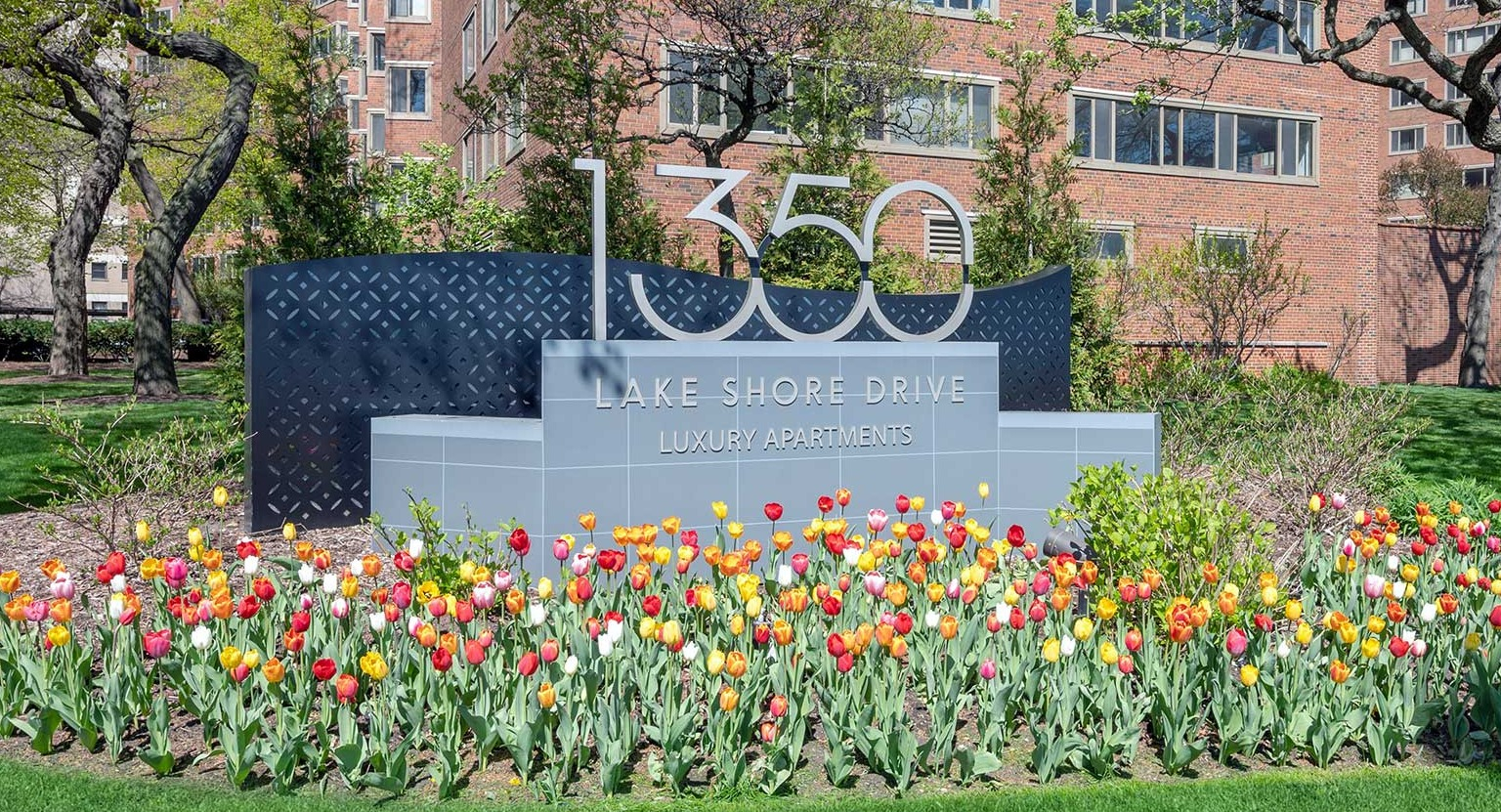 Entrance monument sign for 1350 Lake Shore Drive luxury apartments, framed by blooming tulips and mature trees in Chicago