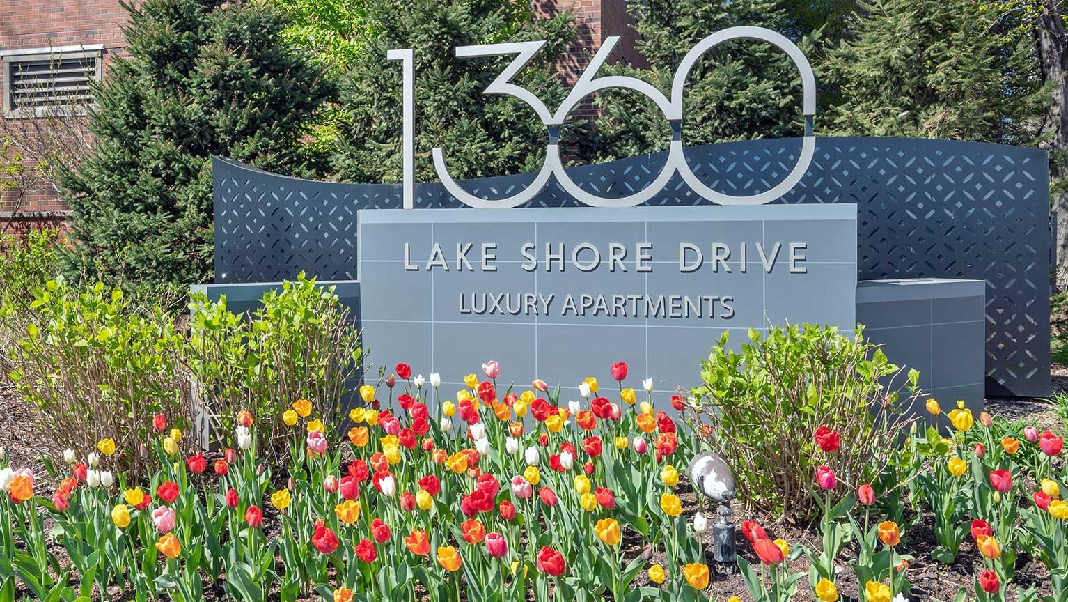 Entrance monument sign for 1360 Lake Shore Drive luxury apartments, surrounded by colorful tulips and landscaped grounds in Chicago