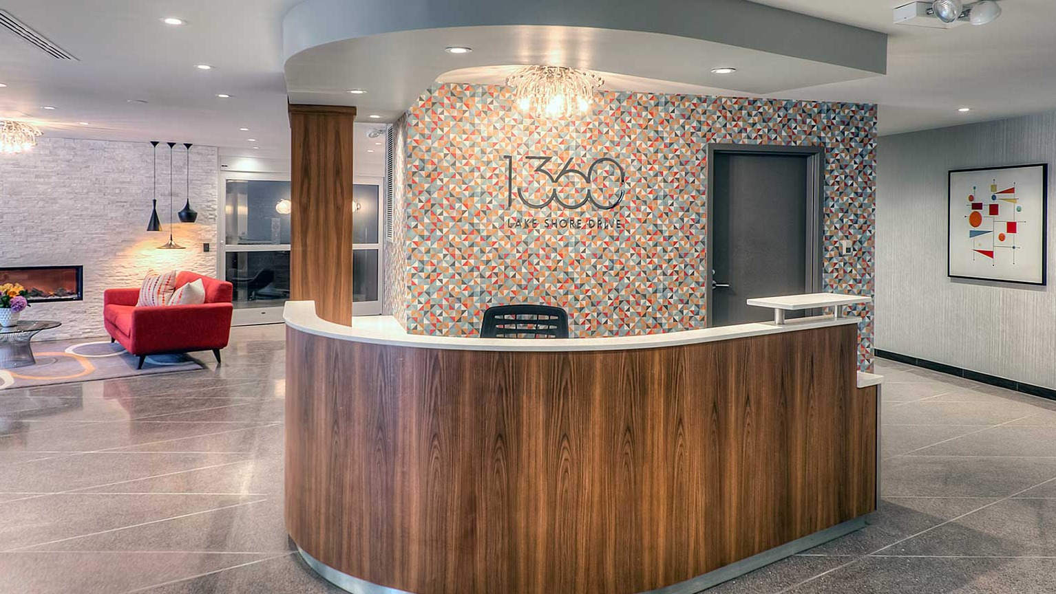 Warm 1360 Lake Shore Drive lobby with curved reception desk, patterned accent wall, and comfortable seating by the fireplace in Chicago