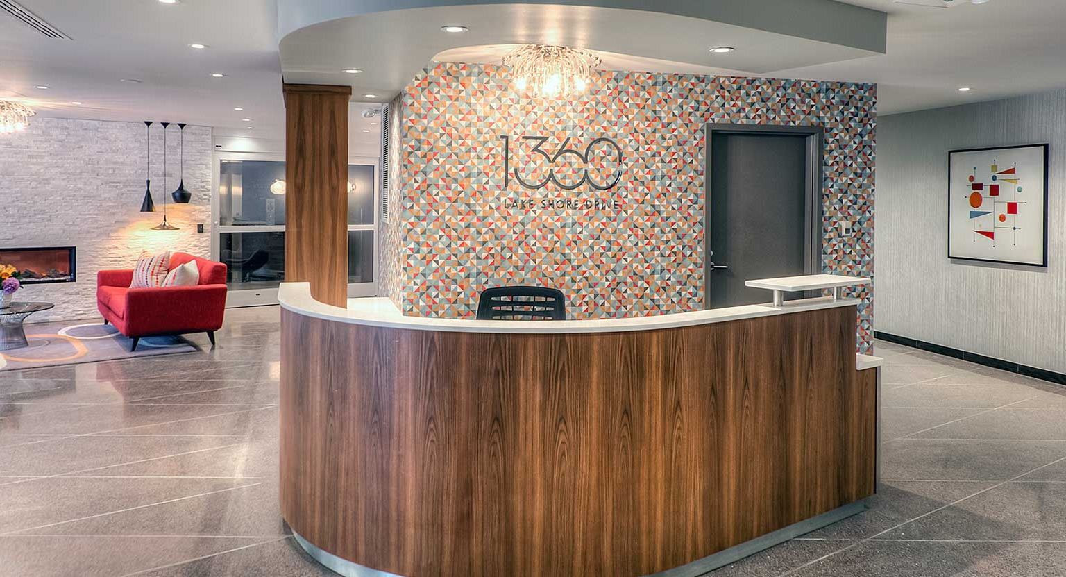 Warm 1360 Lake Shore Drive lobby with curved reception desk, patterned accent wall, and comfortable seating by the fireplace in Chicago