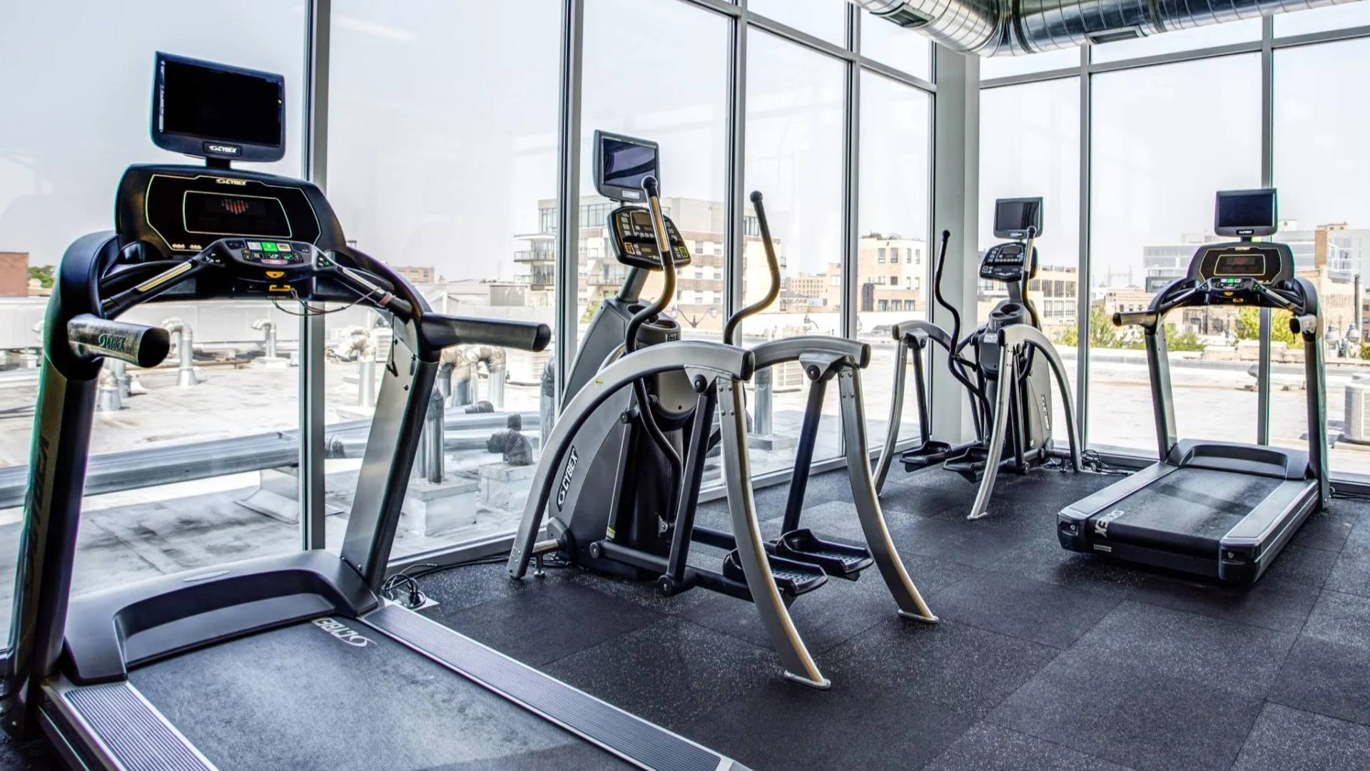Cardio room at 13thirteen Randolph Street Lofts showcasing treadmills, ellipticals, and recumbent bikes beside floor-to-ceiling windows with Chicago views
