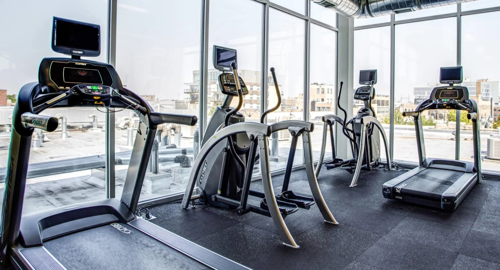 Cardio room at 13thirteen Randolph Street Lofts showcasing treadmills, ellipticals, and recumbent bikes beside floor-to-ceiling windows with Chicago views