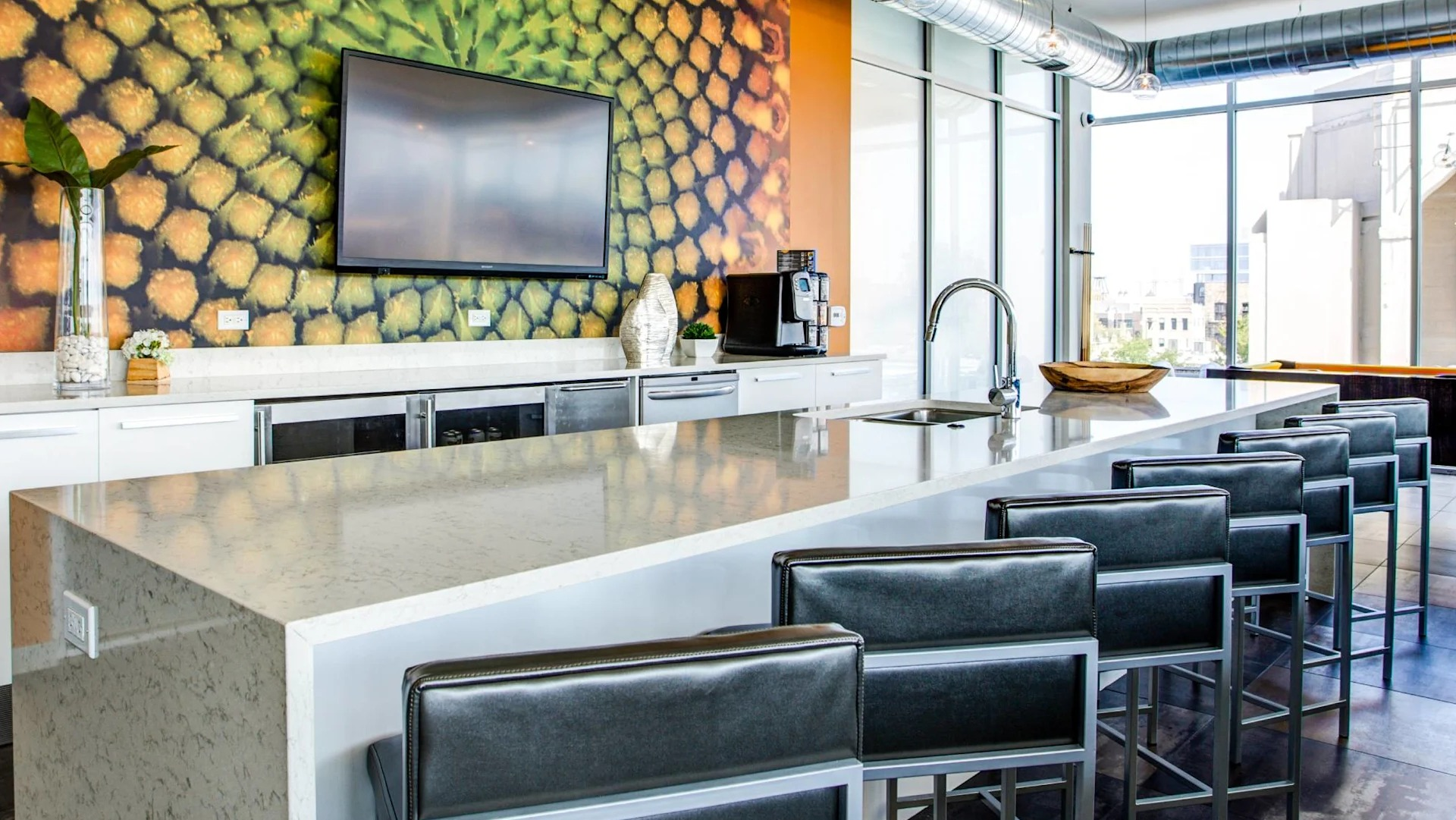 Stylish clubroom kitchen at 13thirteen Randolph Street Lofts with long quartz island, bar seating, TV, and bold accent wall overlooking Chicago views