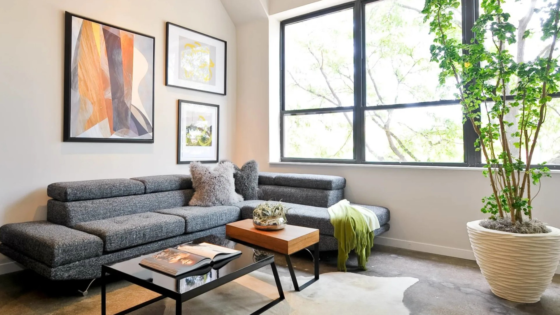 Cozy living area at 13thirteen Randolph Street Lofts with gray sectional, artwork, large windows, and polished concrete floors in Chicago