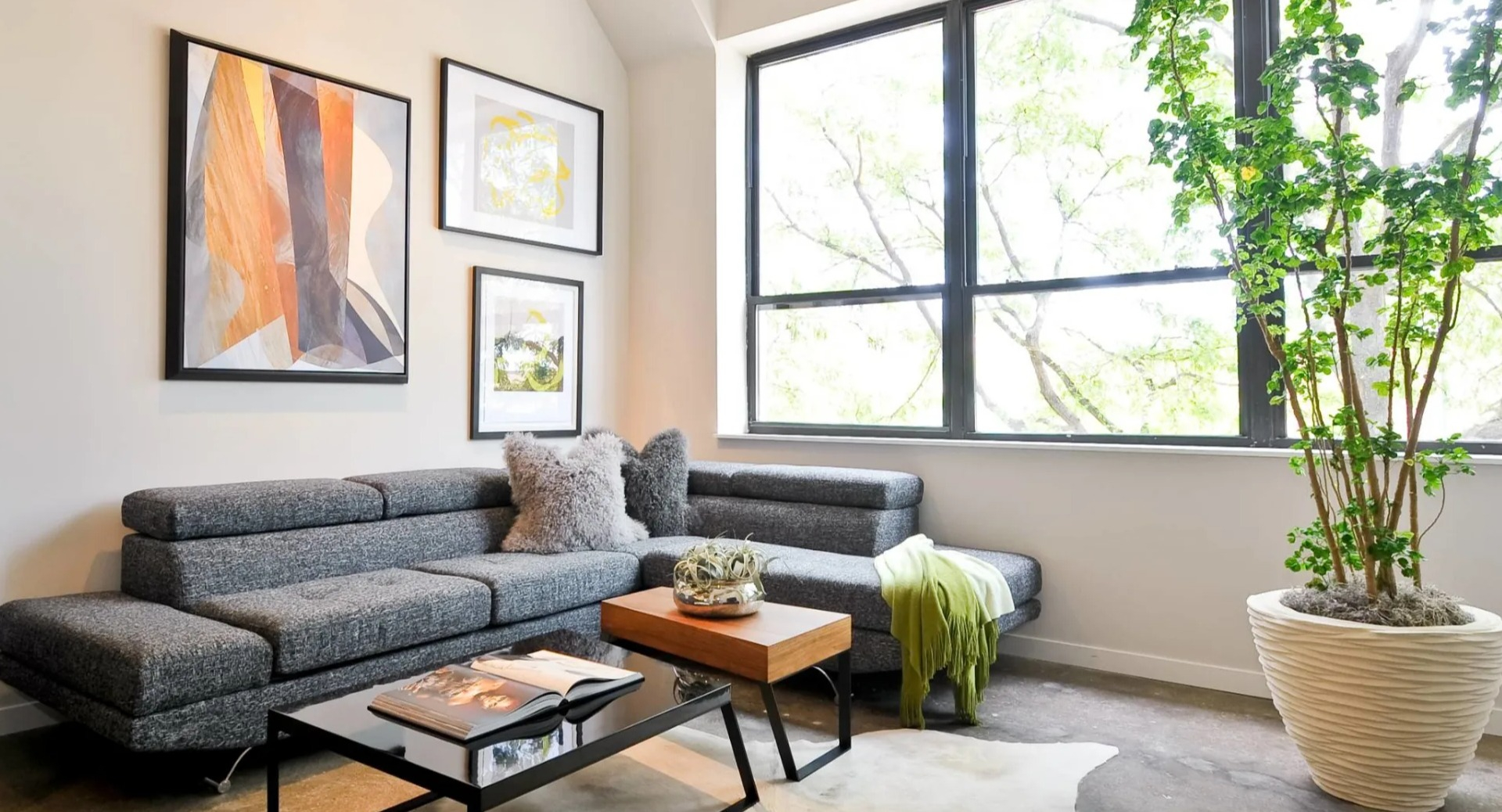 Cozy living area at 13thirteen Randolph Street Lofts with gray sectional, artwork, large windows, and polished concrete floors in Chicago