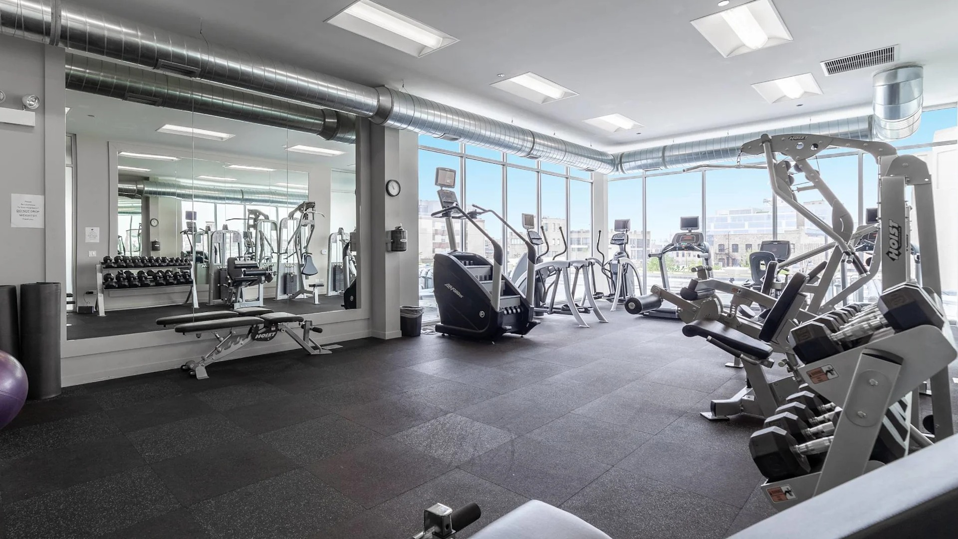 Bright fitness center at 13thirteen Randolph Street Lofts featuring treadmills, ellipticals, free weights, and mirrors with skyline views for Chicago renters